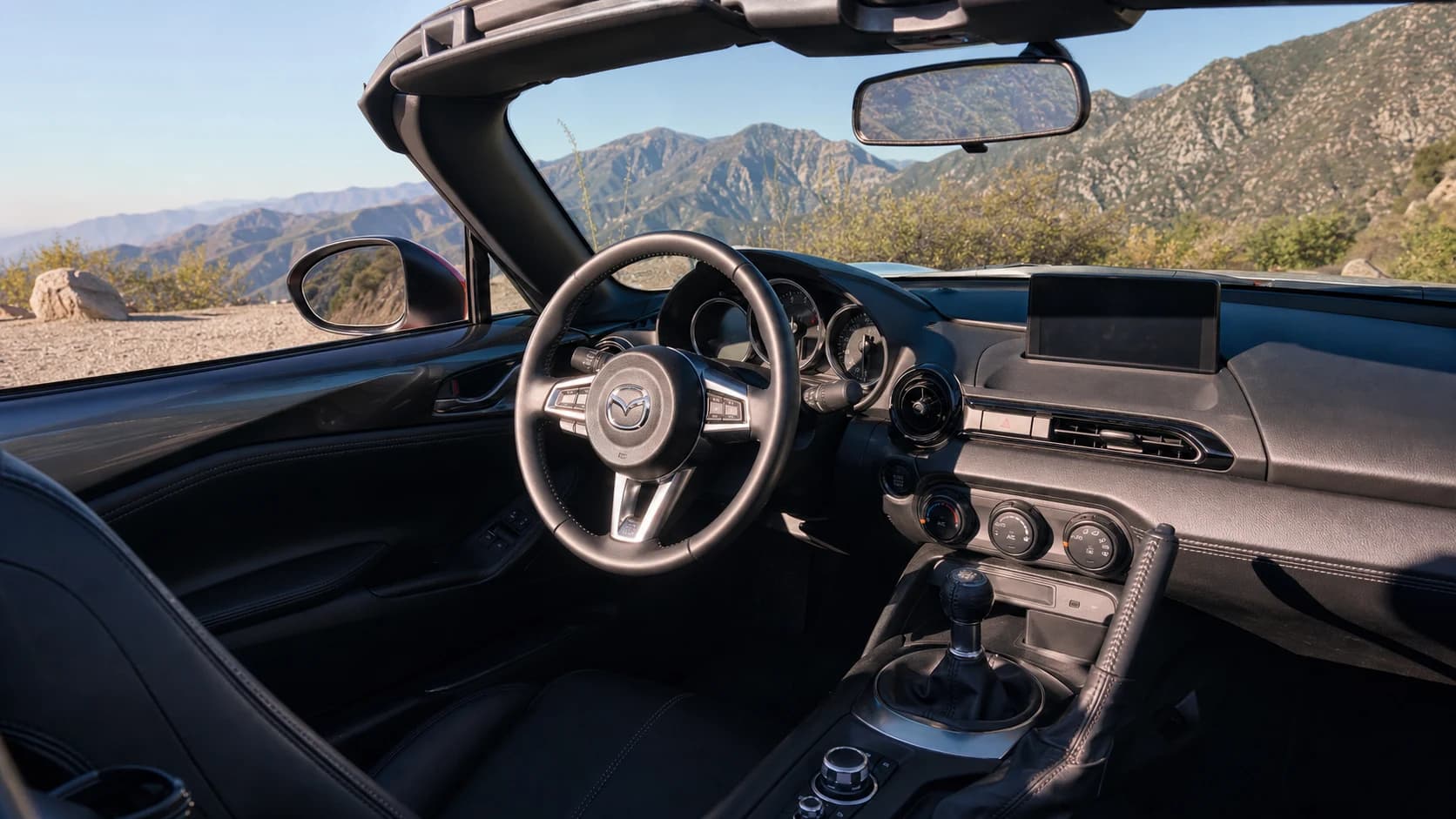 Mazda MX-5 Miata with its roof open on a coastal road
